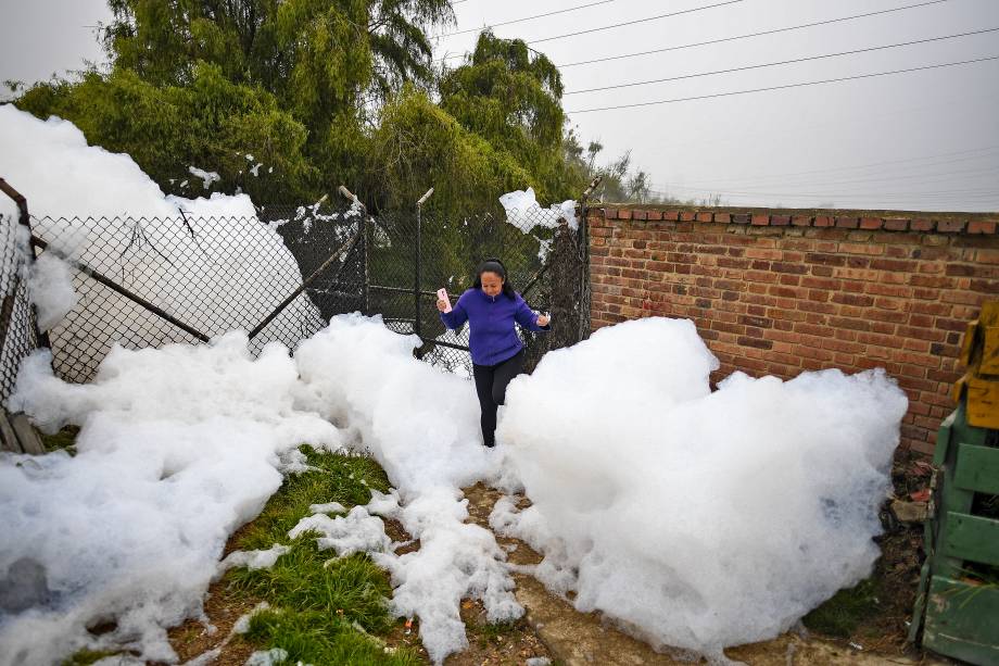 Mulher caminha sobre espuma pungente que se formou em um rio poluído e invadiu o bairro de Los Puentes, em Mosquera, oeste de Bogotá, em 26 de abril de 2022