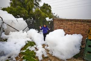 A woman walks through pungent foam which formed in a polluted river and invaded the Los Puentes neighbourhood, in Mosquera, west of Bogota, on April 26, 2022. (Photo by Juan BARRETO / AFP)
