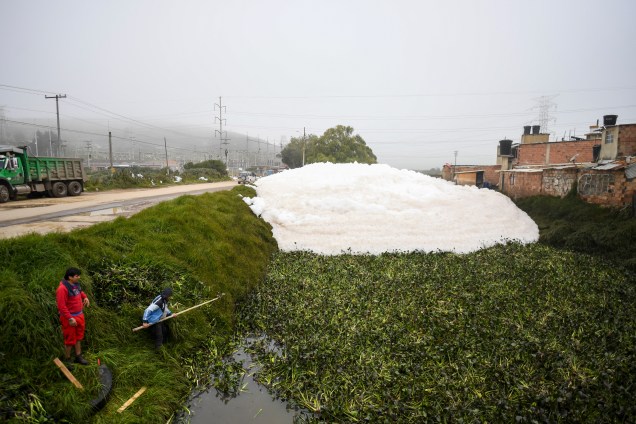 Dois homens estão perto de espuma pungente que se formou em um rio poluído e invadiu o bairro de Los Puentes, em Mosquera, a oeste de Bogotá, em 26 de abril de 2022.
