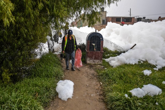 Um homem caminha perto de uma espuma pungente que se formou em um rio poluído e invadiu o bairro de Los Puentes, em Mosquera, a oeste de Bogotá, em 26 de abril de 2022.
