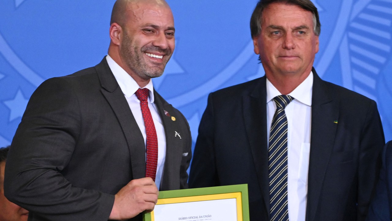 Brazilian President Jair Bolsonaro (R) and deputy Daniel Silveira, pose with a framed copy of the presidential pardon, during an act in defense of freedom of expression at Planalto Palace in Brasilia on April 27, 2022. - Brazilian President Jair Bolsonaro defended his decision to grant a pardon to a controversial ally convicted of attacking democratic institutions, saying "I free people who are innocent." The far-right president has come in for criticism since pardoning Congressman Daniel Silveira, a day after the Supreme Court sentenced the 39-year-old lawmaker to eight years and nine months in prison for his role leading a movement calling for the court to be overthrown. (Photo by EVARISTO SA / AFP)