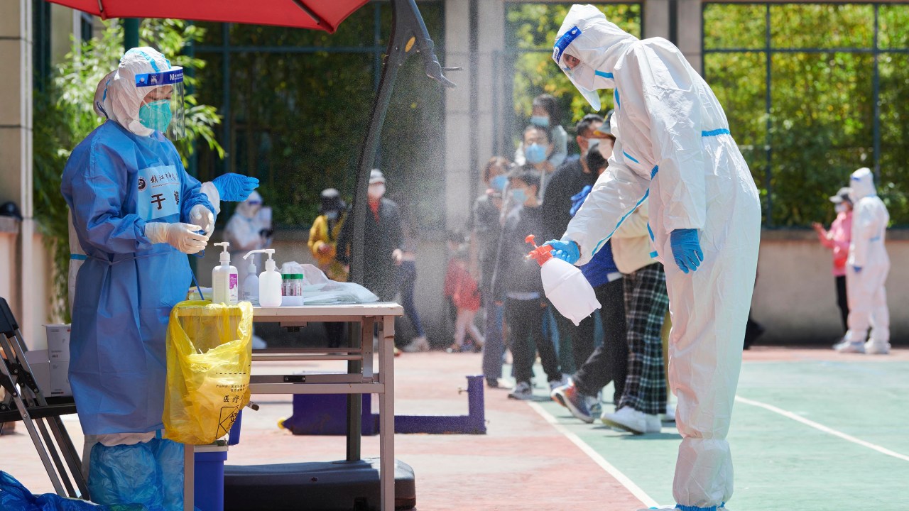 Um voluntário da comunidade usando equipamento de proteção individual desinfeta uma área antes de realizar um teste para o coronavírus Covid-19 em um complexo durante um bloqueio Covid-19 no distrito de Pudong, em Xangai, em 17 de abril de 2022.