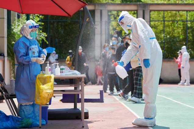 Um voluntário da comunidade usando equipamento de proteção individual desinfeta a área, antes de realizar um teste para o coronavírus Covid-19, no distrito de Pudong, em Xangai.