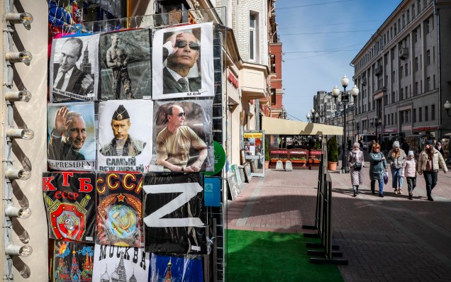 Russos andam na rua e`a frente loja de presentes com camisetas à venda com a letra Z e retratos do presidente russo Vladimir Putin em Moscou, Rússia, 18 de abril de 2022.