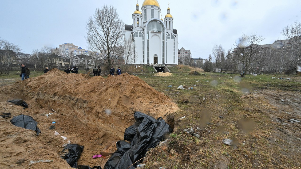 A mass grave is seen behind a church in the town of Bucha, northwest of the Ukrainian capital Kyiv on April 3, 2022. - Ukraine and Western nations on Sunday accused Russian troops of war crimes after the discovery of mass graves and "executed" civilians near Kyiv, prompting vows of action at the International Criminal Court. City mayor Anatoly Fedoruk told AFP that 280 other bodies had been buried in mass graves. One rescue official said 57 people were found in one hastily dug trench behind a church. (Photo by Sergei SUPINSKY / AFP)