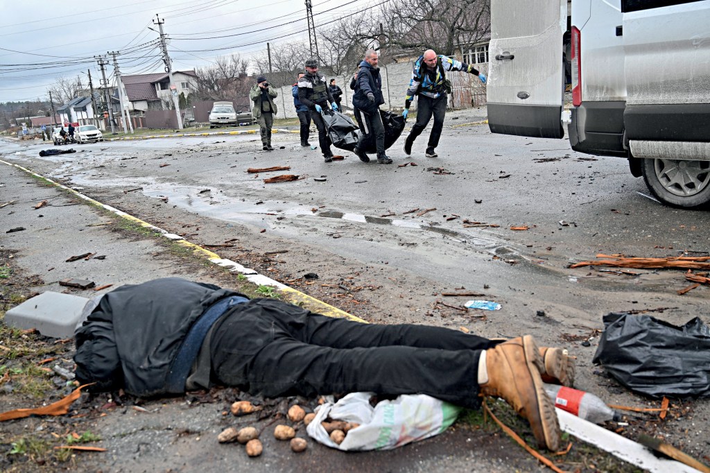 EDITORS NOTE: Graphic content / CAPTION ADDITION - Communal workers carry a civilian in a body bag as another corpse is seen on the ground in the town of Bucha, not far from the Ukrainian capital of Kyiv on April 3, 2022. US and NATO leaders voiced shock and horror at new evidence of atrocities against civilians in Ukraine, and warned that Russian troop movements away from Kyiv did not signal a withdrawal or end to the violence. - The Kremlin on April 4, 2022 rejected accusations that Russian forces were responsible for killing civilians near Kyiv. "We categorically reject all allegations," Kremlin spokesman Dmitry Peskov told journalists. (Photo by Sergei SUPINSKY / AFP)