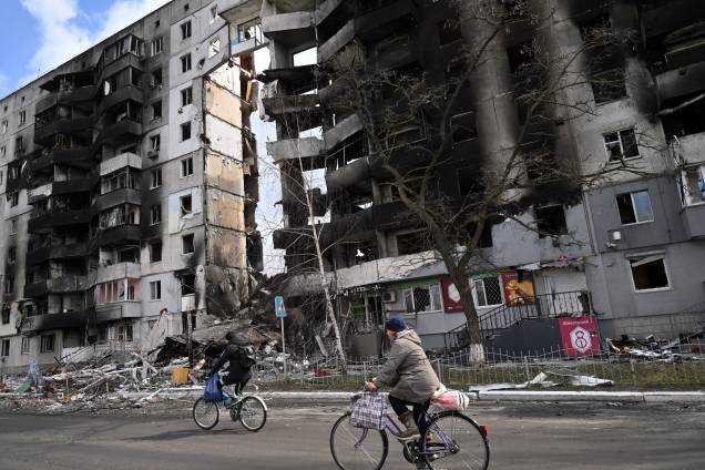 Pessoas andam de bicicleta passando por prédios destruídos na cidade de Borodianka, a noroeste de Kiev -