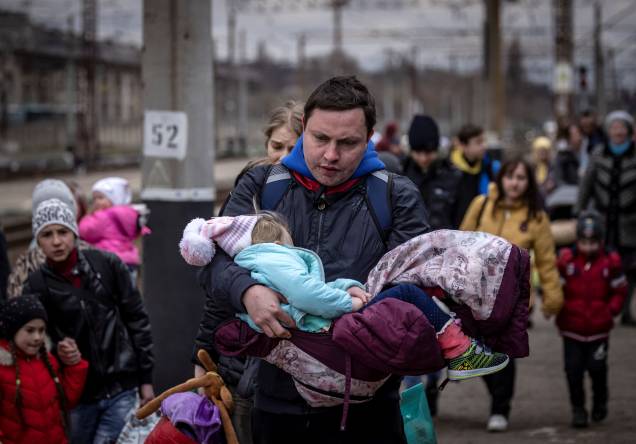 Um homem carrega uma menina ao chegar com outras famílias para embarcar em um trem na estação central de Kramatorsk -