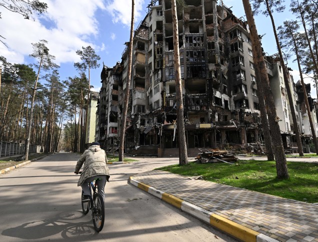Um morador local, passando de bicicleta, tendo ao fundo, prédio residencial destruído em Irpin, a noroeste de Kiev, em 24 de abril de 2022, em meio à invasão russa.