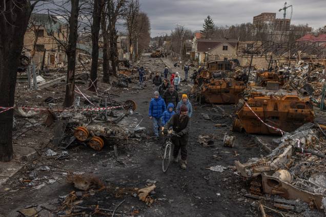 Moradores passam por máquinas militares russas destruídas na rua, em Bucha -