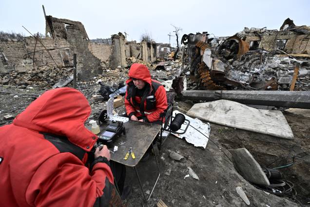 Reparadores restauram cabos de comunicação local entre os destroços de veículos blindados e edifícios destruídos em uma rua na cidade de Bucha, nos arredores da capital ucraniana Kiev -