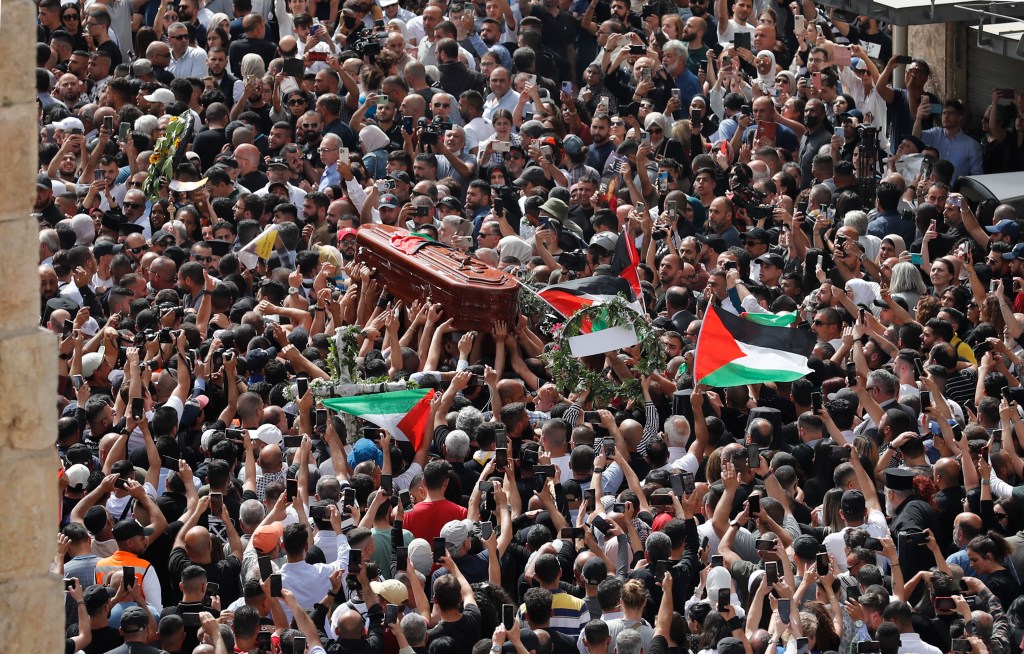 Palestinian mourners wave national flags as they carry the casket of slain Al-Jazeera journalist Shireen Abu Akleh, during her funeral procession near Jaffa Gate, one of the main gates of the Old City of Jerusalem, on May 13, 2022. - Abu Akleh, who was shot dead on May 11, 2022 while covering a raid in the Israeli-occupied West Bank, was among Arab media's most prominent figures and widely hailed for her bravery and professionalism. (Photo by Ahmad GHARABLI / AFP)
