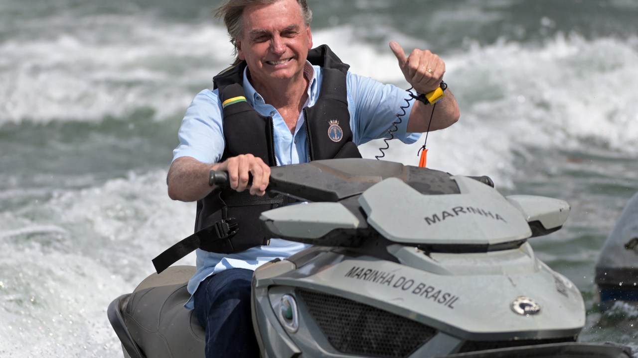 Brazilian President Jair Bolsonaro rides a jet ski as he gives a thumbs up at supporters taking part in a boat ride on Paranoa Lake in Brasilia, on May 15, 2022. (Photo by EVARISTO SA / AFP)