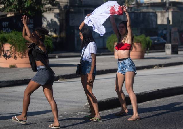 Mulheres segurando uma camiseta ensanguentada gritam com policiais do lado de fora do Hospital Getulio Vargas -