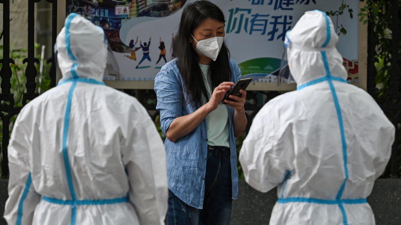 Workers wearing protective gear talk with a woman on a street during a Covid-19 coronavirus lockdown in the Jing'an district of Shanghai on May 25, 2022.
