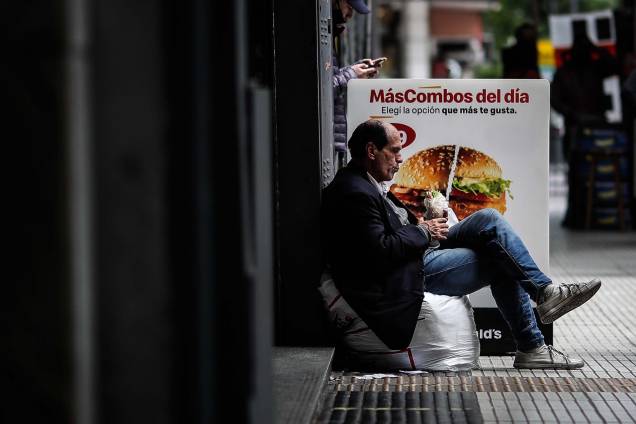 Um homem em situação de rua se alimenta em frente `a um fast food, em Buenos Aires, na Argentina.