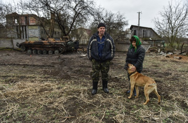 Moradores locais acariciam um cachorro próximo de uma casa destruída na vila de Ivanivka, região de Chernihiv, Ucrânia, 20 de abril de 2022.