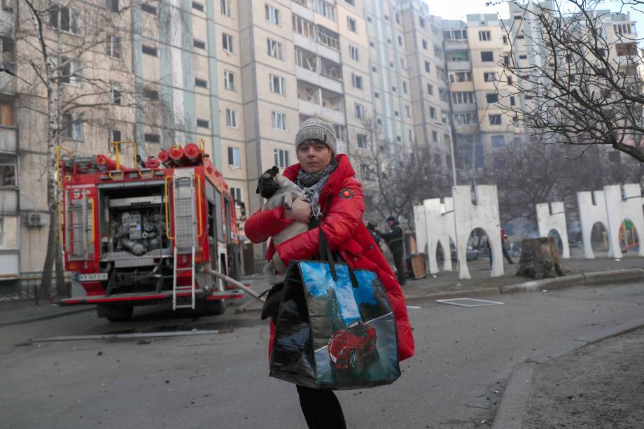 Uma mulher segurando um cachorro se afasta de um prédio atingido por mísseis russos em Kiev, Ucrânia, 20 de março de 2022.