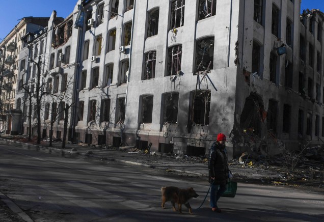 Uma pessoa passeia com um cachorro ao lado de um prédio danificado após bombardeio russo em Kharkiv, Ucrânia, 20 de março de 2022.