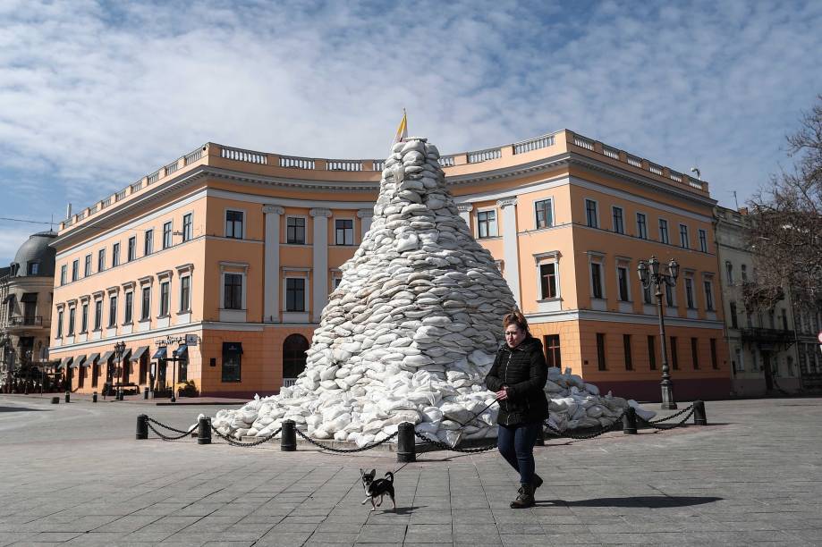 Mulher ucraniana caminha com seu cachorro ao lado do monumento do Duque de Richelieu, protegido pelos bombardeios russos na cidade de Odessa, no sul da Ucrânia, em 21 de março de 2022.