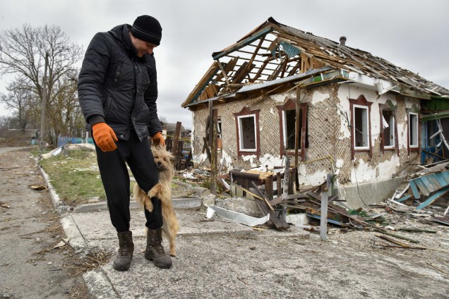 Um homem brinca com um cachorro ao lado de uma casa bombardeada em Kukhari, Kyiv Oblast, Ucrânia, 16 de abril de 2022.