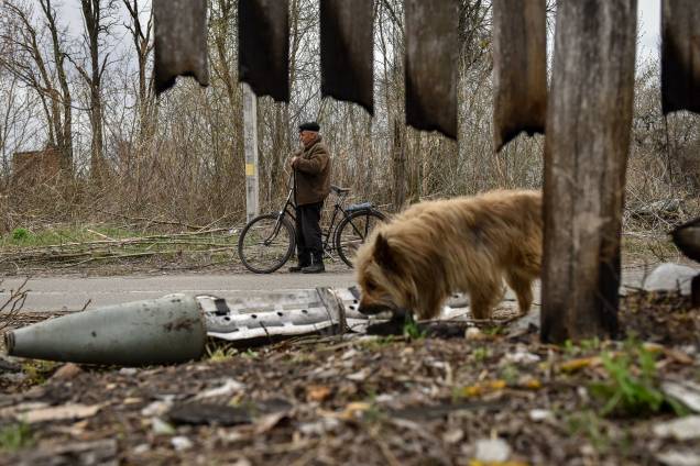 Um homem observa os destroços de um míssil enquanto um cachorro passa, Kukhari, Kiev Oblast, Ucrânia, 16 de abril de 2022. Um homem observa os destroços de um míssil enquanto um cachorro passa, Kukhari, Kiev Oblast, Ucrânia, 16 de abril de 2022.