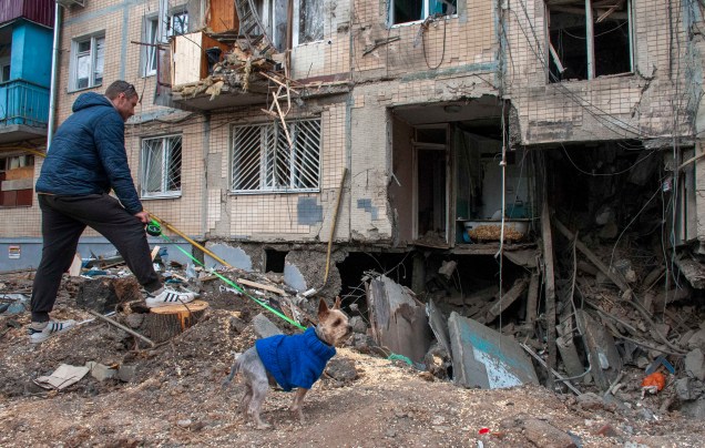 Um homem com um cachorro observa uma entrada destruída em um prédio residencial em Kharkiv, Ucrânia, 10 de abril de 2022.