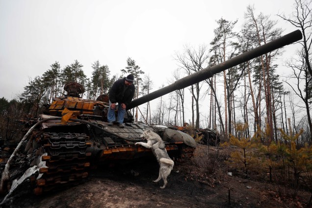 Um ucraniano com seu cachorro inspeciona a destruição de um tanque russo, após a retomada da vila de Dmitrivka, nas proximidades de Kiev, Ucrânia, 02 de abril de 2022.
