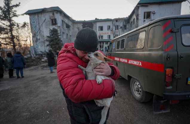 Um homem local abraça um cachorro em frente ao prédio destruído do hospital local no centro de Volnovakha, Ucrânia, 26 de março de 2022.