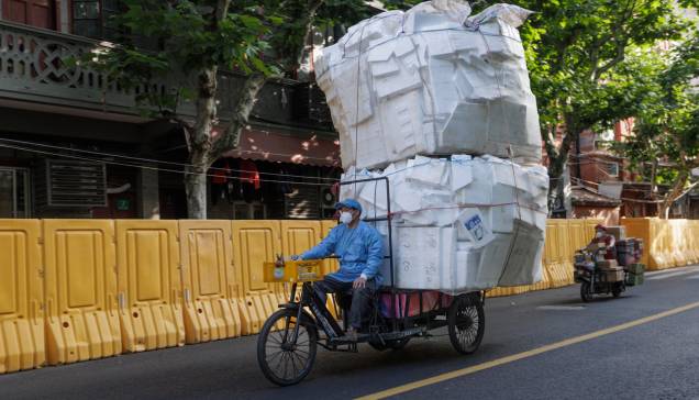 Um homem pilota uma motocicleta de carga carregada com caixas de isopor vazias passando por barreiras antes de um levantamento de bloqueio em Xangai, China, 31/05/2022.
