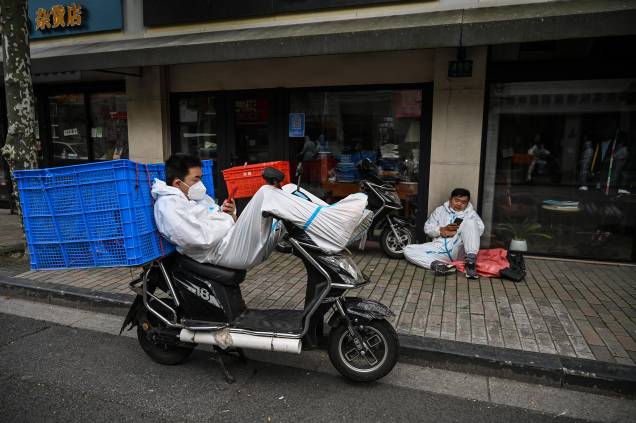 Trabalhadores de entrega usando equipamentos de proteção, descansam em uma rua durante um bloqueio de Coronavírus Covid-19, no distrito de Jing'an, em Xangai, em 25/05/2022.