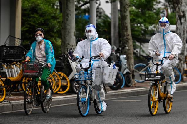 Trabalhadores usando equipamentos de proteção, andam de bicicleta em uma rua durante um bloqueio de Coronavírus Covid-19 no distrito de Jing'an, em Xangai, em 29/05/2022.