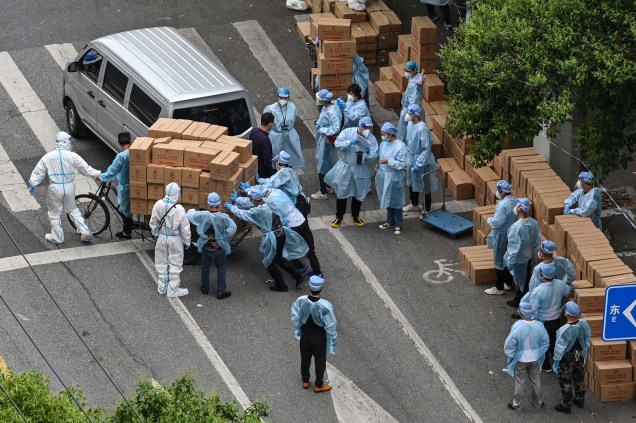 Trabalhadores usando equipamentos de proteção, empurram um carrinho cheio de caixas com alimentos para serem entregues em um bairro durante um bloqueio de Coronavírus Covid-19 no distrito de Jing'an, em Xangai, em 7 de maio de 2022.