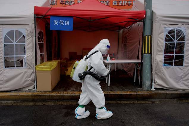 Um trabalhador usando equipamento de proteção individual, desinfeta a entrada de uma área residencial bloqueada devido aos recentes surtos de coronavírus Covid-19 em Pequim em 10 de maio de 2022.