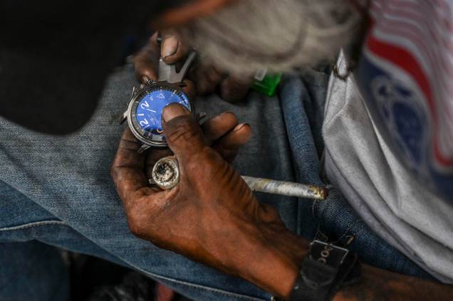 Um homem conserta um relógio enquanto segura um cachimbo de crack, cocaína  misturada com pasta de coca e outras substâncias, no centro de Medellín, Colômbia, em 25 de fevereiro de 2022.