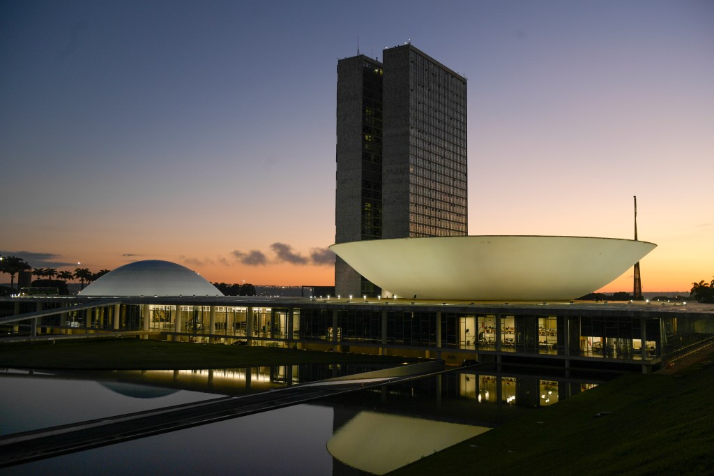 Fachada do Congresso Nacional, a sede das duas Casas do Poder Legislativo brasileiro, durante o amanhecer. As cúpulas abrigam os plenários da Câmara dos Deputados (côncava) e do Senado Federal (convexa), enquanto que nas duas torres - as mais altas de Brasília, com 100 metros - funcionam as áreas administrativas e técnicas que dão suporte ao trabalho legislativo diário das duas instituições. Obra do arquiteto Oscar Niemeyer