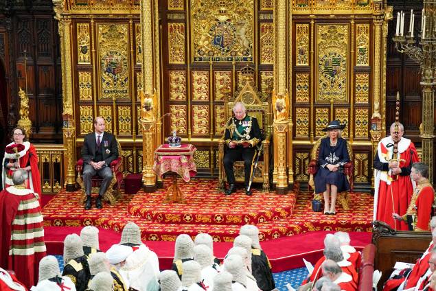 O príncipe britânico Charles, Príncipe de Gales, lê o Discurso da Rainha sentado ao lado da Coroa do Estado Imperial da Grã-Bretanha, Camilla Duquesa da Cornualha e do Britânico Príncipe William, Duque de Cambridge na Câmara dos Lordes, durante a Abertura Estadual do Parlamento, em Londres, em 10 de maio de 2022.