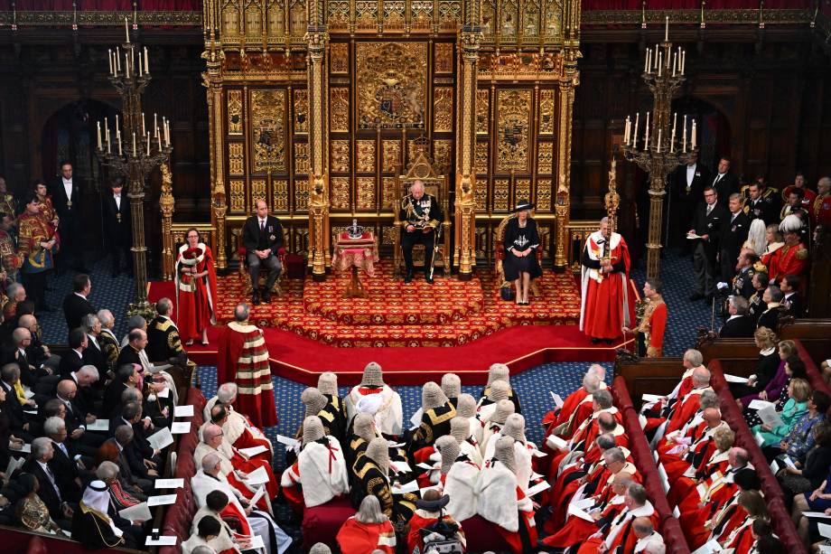 O príncipe britânico Charles, Príncipe de Gales, lê o Discurso da Rainha sentado ao lado da Coroa do Estado Imperial da Grã-Bretanha, Camilla Duquesa da Cornualha e do Britânico Príncipe William, Duque de Cambridge na Câmara dos Lordes, durante a Abertura Estadual do Parlamento, em Londres, em 10 de maio de 2022.