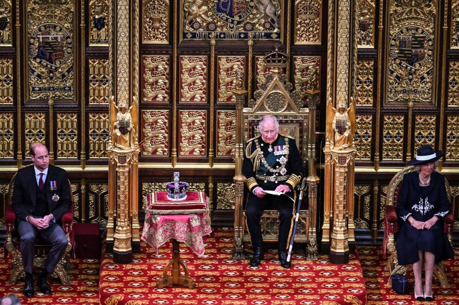 O príncipe britânico Charles, Príncipe de Gales, lê o Discurso da Rainha sentado ao lado da Coroa do Estado Imperial da Grã-Bretanha, Camilla Duquesa da Cornualha e do Britânico Príncipe William, Duque de Cambridge na Câmara dos Lordes, durante a Abertura Estadual do Parlamento, em Londres, em 10 de maio de 2022.