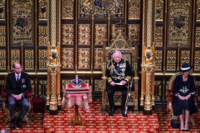 O príncipe britânico Charles, Príncipe de Gales, lê o Discurso da Rainha sentado ao lado da Coroa do Estado Imperial da Grã-Bretanha, Camilla Duquesa da Cornualha e do Britânico Príncipe William, Duque de Cambridge na Câmara dos Lordes, durante a Abertura Estadual do Parlamento, em Londres, em 10 de maio de 2022.