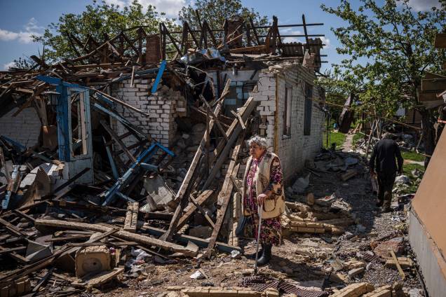 Um casal traz sua bagagem para fora de sua casa destruída na vila de Vilkhivka, perto da cidade oriental de Kharkiv, em 14 de maio de 2022.