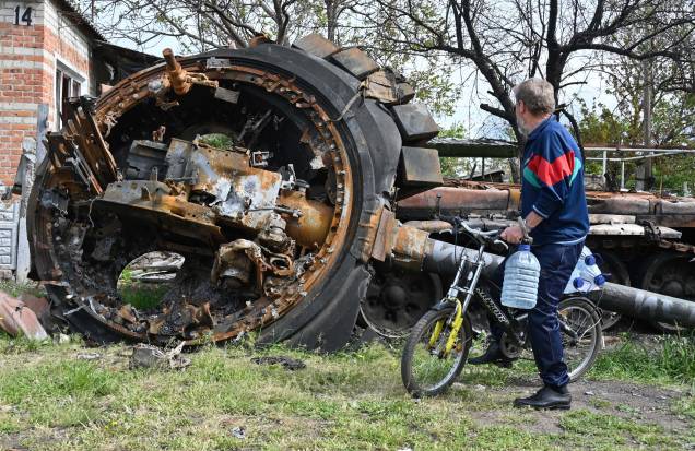 Um morador local, observa um tanque russo destruído ao lado de uma casa residencial na vila de Mala Rogan, a leste de Kharkiv, em 15 de maio de 2022, em meio à invasão russa da Ucrânia.