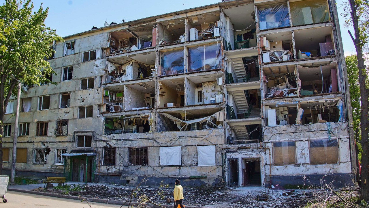 Kharkiv (Ucrânia), 12/05/2022.- Uma mulher passa por um edifício residencial danificado durante o bombardeio de Kharkiv, Ucrânia, 12 de maio de 2022. O Ministério da Defesa da Ucrânia anunciou em 10 de maio que as tropas ucranianas haviam recapturado Kharkiv e aldeias ao norte e nordeste da cidade das forças russas e os empurrou de volta para a fronteira. A cidade de Kharkiv, a segunda maior da Ucrânia, testemunhou repetidos ataques aéreos das forças russas. Em 24 de fevereiro, tropas russas invadiram o território ucraniano iniciando um conflito que provocou destruição e uma crise humanitária. (Rússia, Ucrânia) EFE/EPA/SERGEY KOZLOV