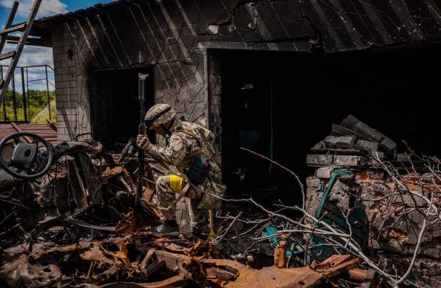 Um soldado da unidade de forças especiais ucranianas, passa por destroços na aldeia de Rus'ka Lozova, ao norte de Kharkiv, em 16 de maio de 2022.