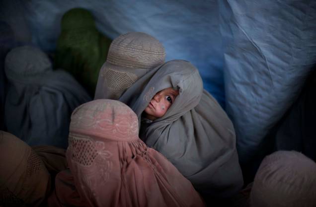 Uma criança Afegã, observa mulheres cobertas com burcas nos arredores de Cabul, Afeganistão.