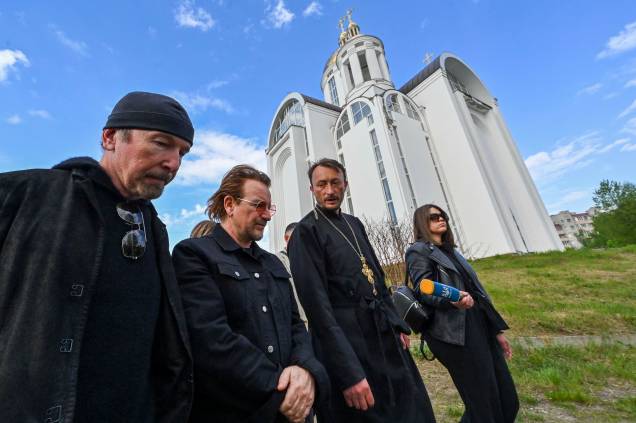 Andrii Holovine, sacerdote da Igreja de St. Andrew Pervozvannoho All Saints, Bono(Paul David Hewson), ativista e líder da banda de rock irlandesa U2 e o guitarrista David Howell Evans, 'The Edge', caminham em frente`a uma igreja ortodoxa na cidade ucraniana de Bucha, próximo de Kiev, em 8 de maio de 2022.