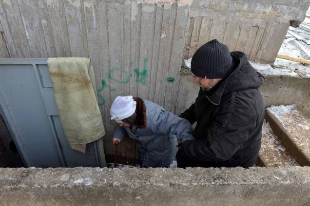 Um homem auxilia uma idosa a se abrigar no porão de um prédio, depois que tropas russas bombardearam a área na segunda maior cidade ucraniana de Kharkiv, no leste do país.