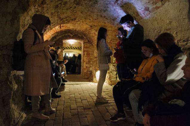Pessoas se acomodam num porão de um edifício histórico que está sendo usado como abrigo antiaéreo durante um alerta de ataque aéreo na cidade de Lviv, no oeste da Ucrânia.