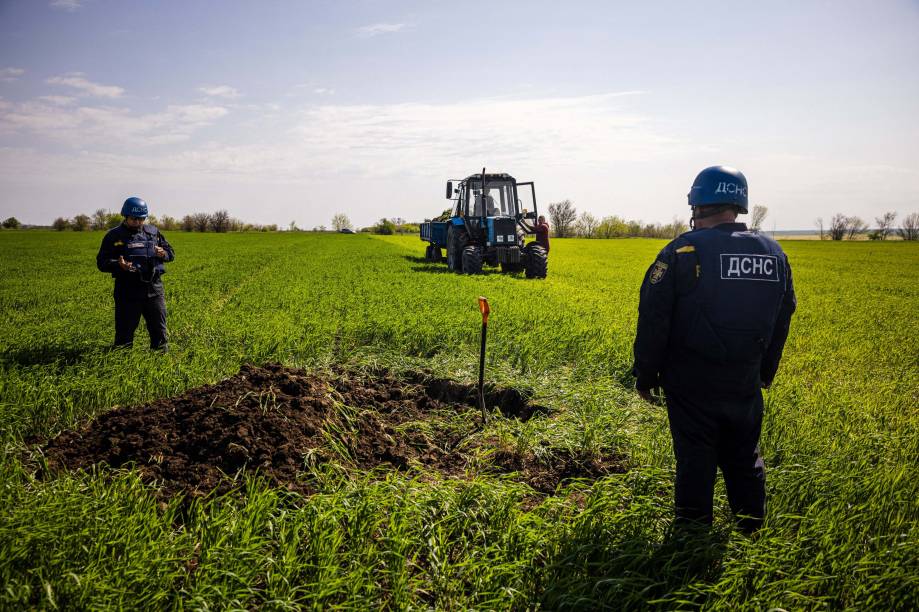 Plantação e membros de uma equipe de desminagem do Serviço de Emergência do Estado da Ucrânia se preparam para destruir um míssil não detonado que permanece perto da vila de Hryhorivka, região de Zaporizhzhia, em 5 de maio de 2022, em meio à invasão russa na Ucrânia.