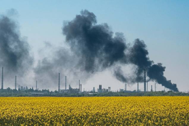 Plantação aflorando e ao fundo, fumaça após o bombardeio numa refinaria de petróleo próximo de Lysychansk, leste da Ucrânia, em 9 de maio de 2022, na invasão russa na Ucrânia.